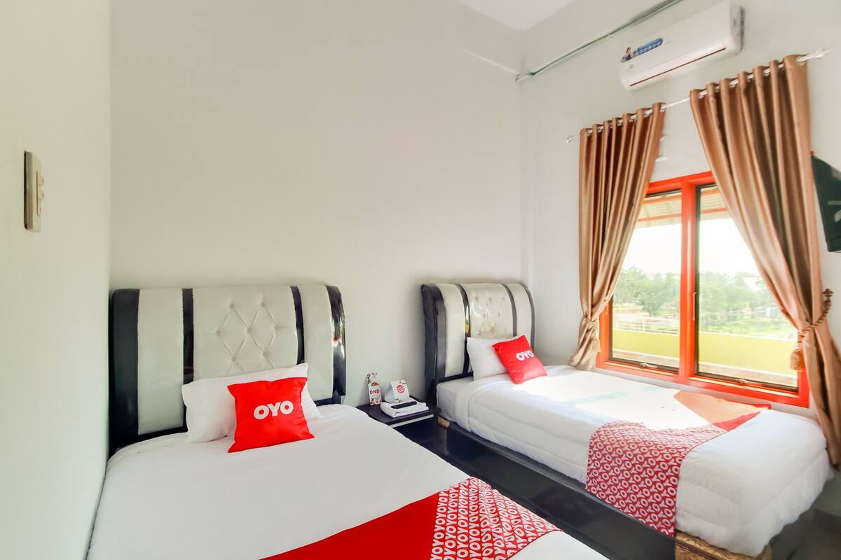 Hotellihuone, jossa on kaksi sänkyä, ja molemmissa on punavalkoinen päiväpeite. Huoneessa on myös ikkuna, jossa on verhot.