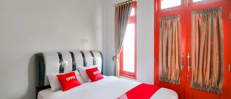 A hotel room with a bed, a red door, and curtains.