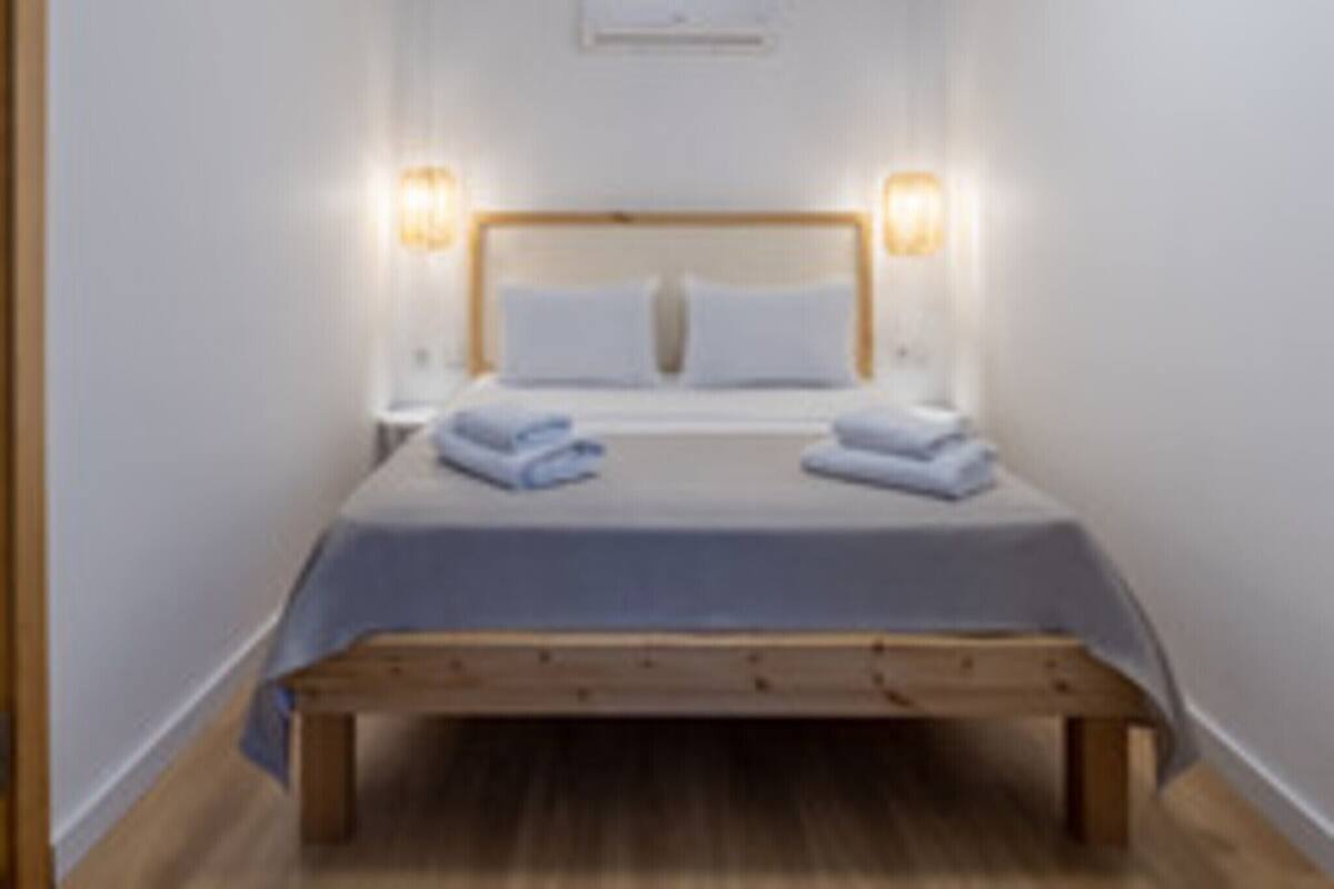 A single bed with a wooden headboard, two bedside lamps, and a wall-mounted air conditioner.