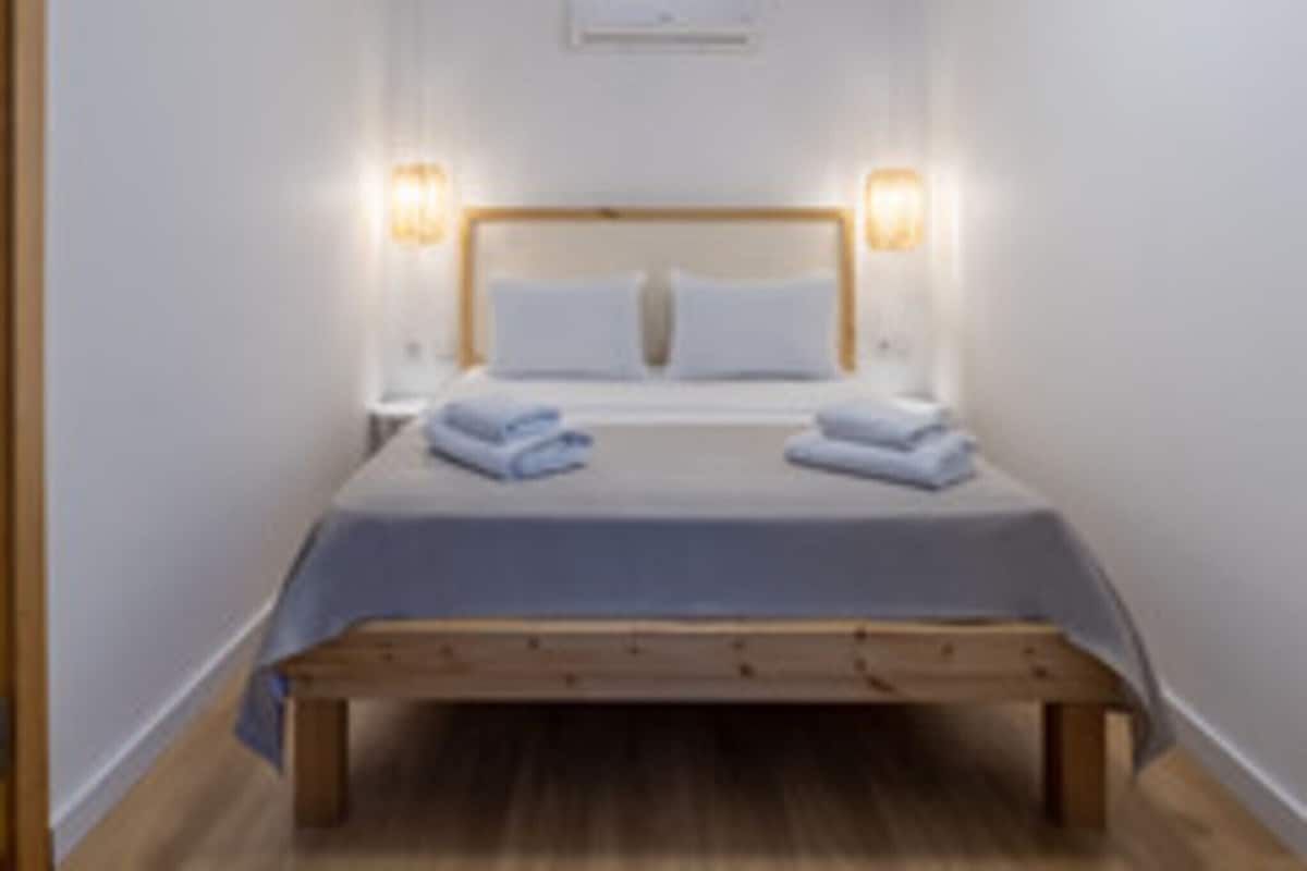 Una cama individual con cabecera de madera, dos lámparas de noche y un aire acondicionado instalado en la pared.
