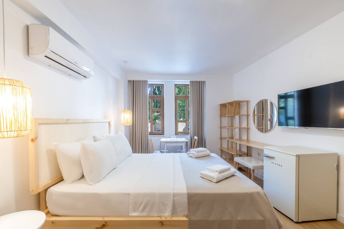 A modern hotel room with a large bed, a TV, a mini-fridge, and a view of the outdoors.