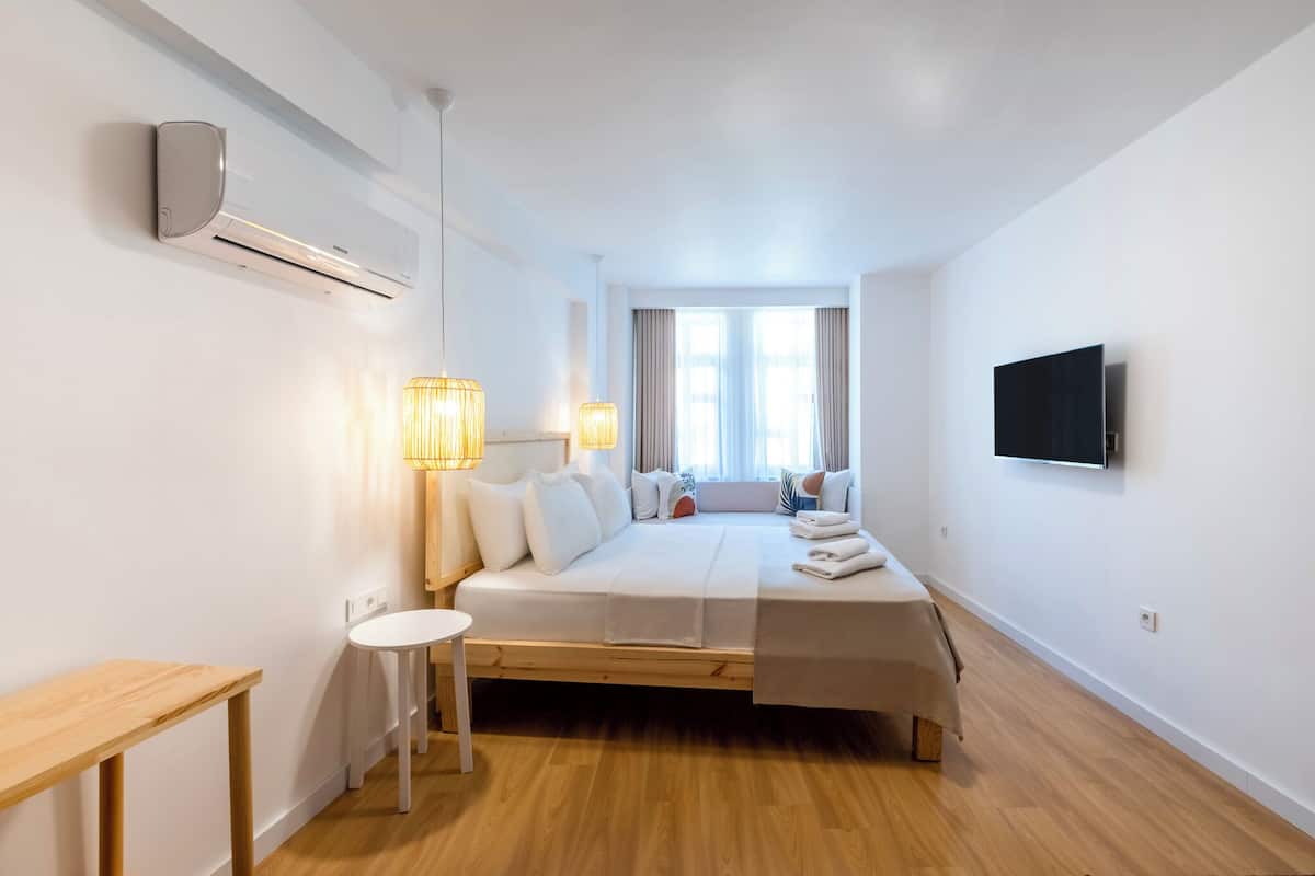 A minimalist hotel room with a bed, bedside lamps, a TV, and a window with curtains.