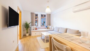 A modern living room with a sofa, a dining table, and a TV mounted on the wall. - Audo Studio Hotel (Antalya)