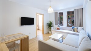A modern living room with a flat-screen TV, a white sofa, a coffee table, and a potted plant. - Audo Studio Hotel (Antalya)
