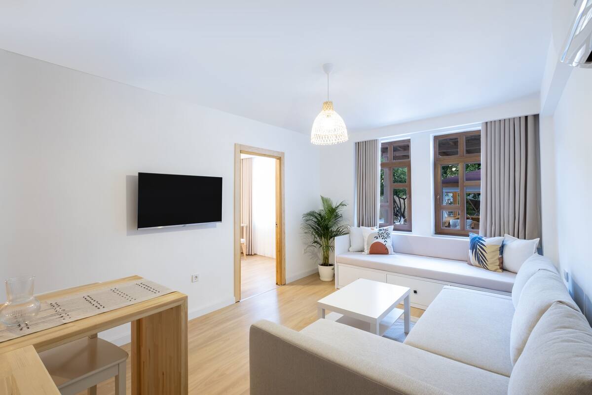 A modern living room with a flat-screen TV, a white sofa, a coffee table, and a potted plant.