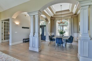 A spacious dining area with a large wooden table, blue upholstered chairs, and a chandelier.