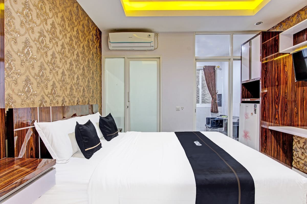 A hotel room with a bed, a TV, an air conditioning unit, and a wardrobe.