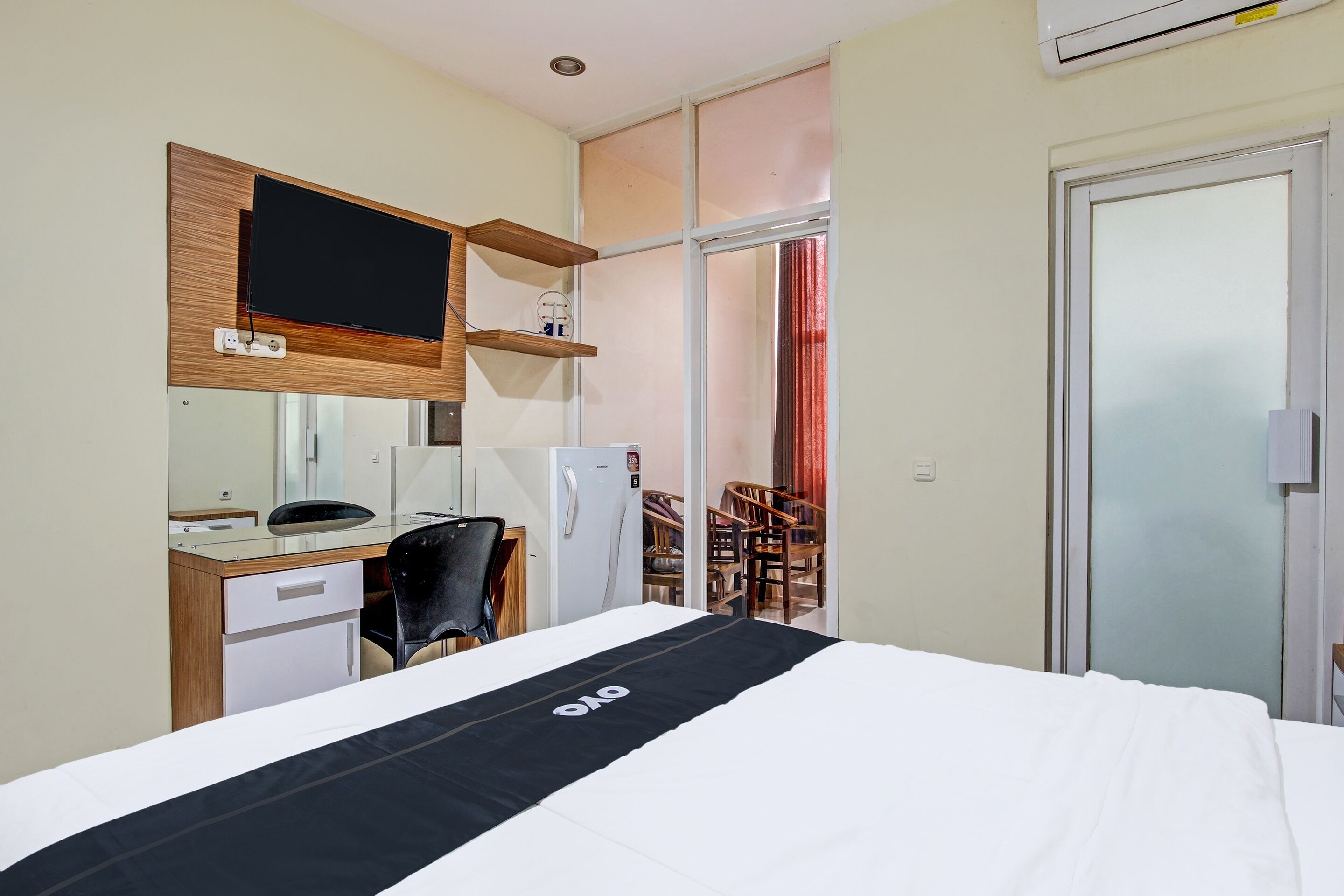 Habitación de hotel con cama, escritorio con computadora, silla, televisor montado en la pared y puerta corredera que da a un balcón.