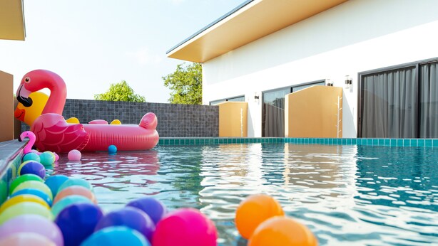 A swimming pool with inflatable flamingo and colorful balls, surrounded by a modern building with large windows and a covered patio area. - Fresh Resort Pattaya (Pattaya)