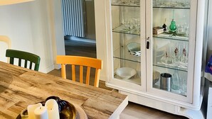 A dining area with a wooden table, chairs, and a cabinet with glass doors displaying glassware.