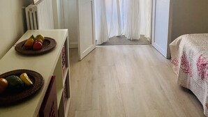 A room with a bed, a table with fruit, and a door leading to a balcony.