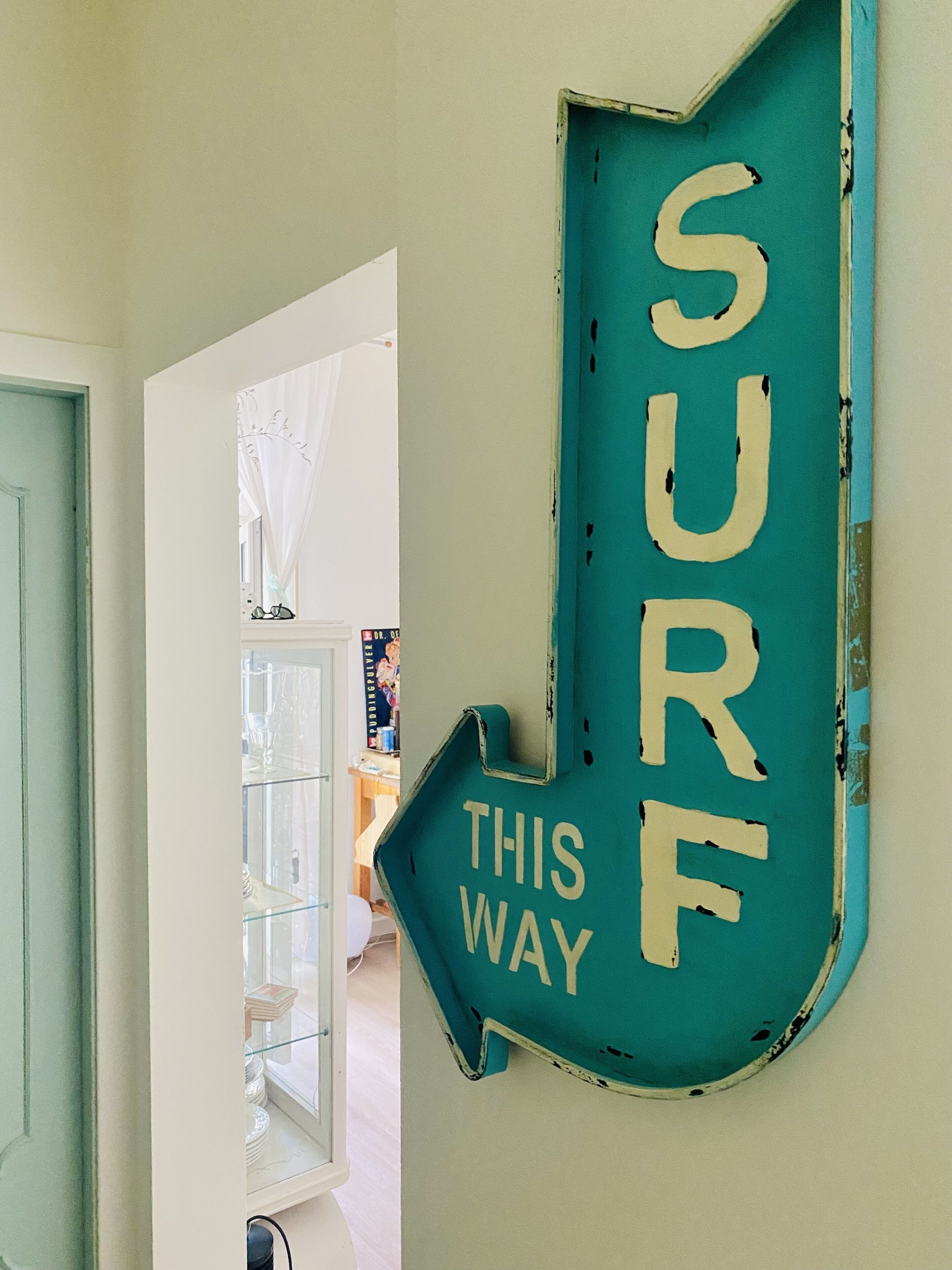 Ein türkisnes Schild mit der Aufschrift 'SURF THIS WAY' an einer Wand befestigt.