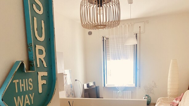 A room with a bed, a desk, a window, and a sign that reads "SURF THIS WAY".