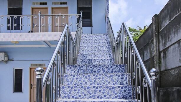 A staircase with blue and white patterned tiles, metal railings, and a building with a door and windows in the background. - OYO Life 90433 Serasi Kost (Palembang)