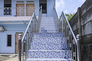 A staircase with blue and white patterned tiles, metal railings, and a building with a door and windows in the background.