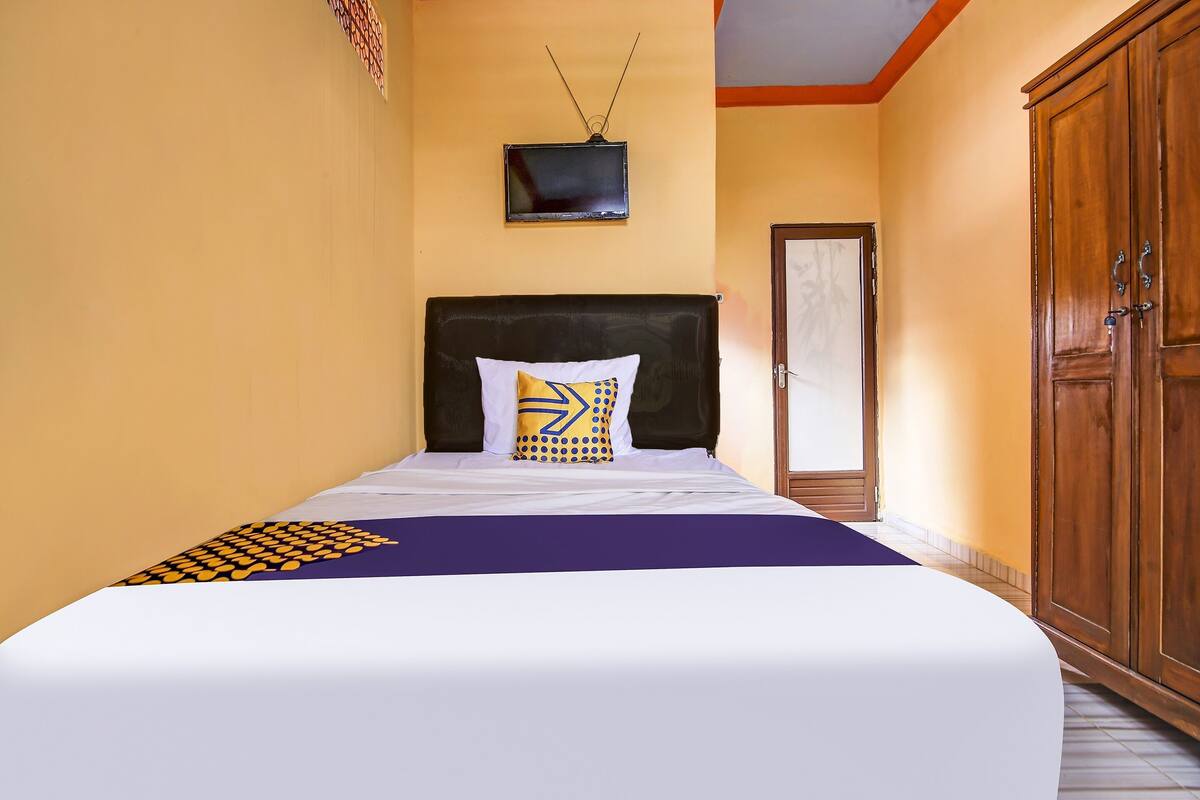 A neatly made bed with a patterned bedspread, a television mounted on the wall, and a wooden wardrobe.