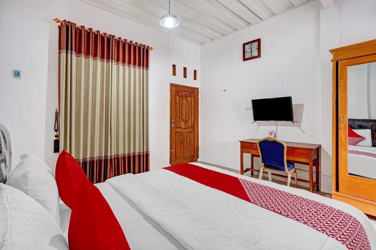 Ein Hotelzimmer mit einem Bett, einem Schreibtisch mit Stuhl, einem Fernseher und einer Holztür.
