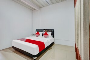 Un lit bien fait, avec une couvre-lit blanche et rouge, une tête de lit noire et deux coussins décoratifs.