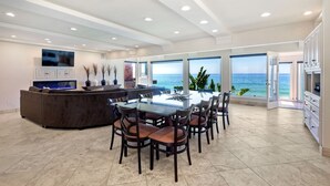 A spacious living area with a large dining table, comfortable seating, a built-in kitchen, and a view of the ocean. - Oceanfront, Hot Tub, Private Beach, Fire Pit (Oceanside)