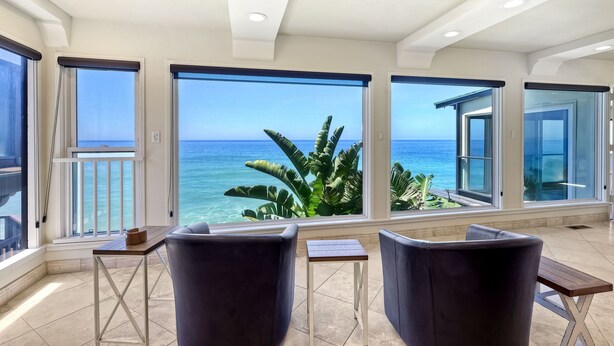 A spacious balcony with large windows offering a view of the ocean and tropical plants. - Oceanfront, Hot Tub, Private Beach, Fire Pit (Oceanside)