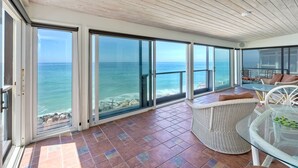 A spacious balcony with large glass doors, wicker furniture, and a view of the ocean. - Oceanfront, Hot Tub, Private Beach, Fire Pit (Oceanside)