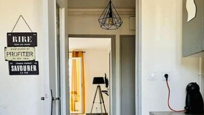 A modern kitchen with white cabinets, a stainless steel countertop, and a hanging light fixture. - F3 Lumineux Tout Équipé sur la Route des Plages (Perpignan)