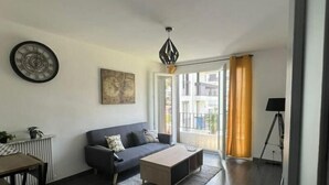A modern living room with a dark wood floor, a grey sofa, a wooden coffee table, and a black pendant light. - F3 Lumineux Tout Équipé sur la Route des Plages (Perpignan)