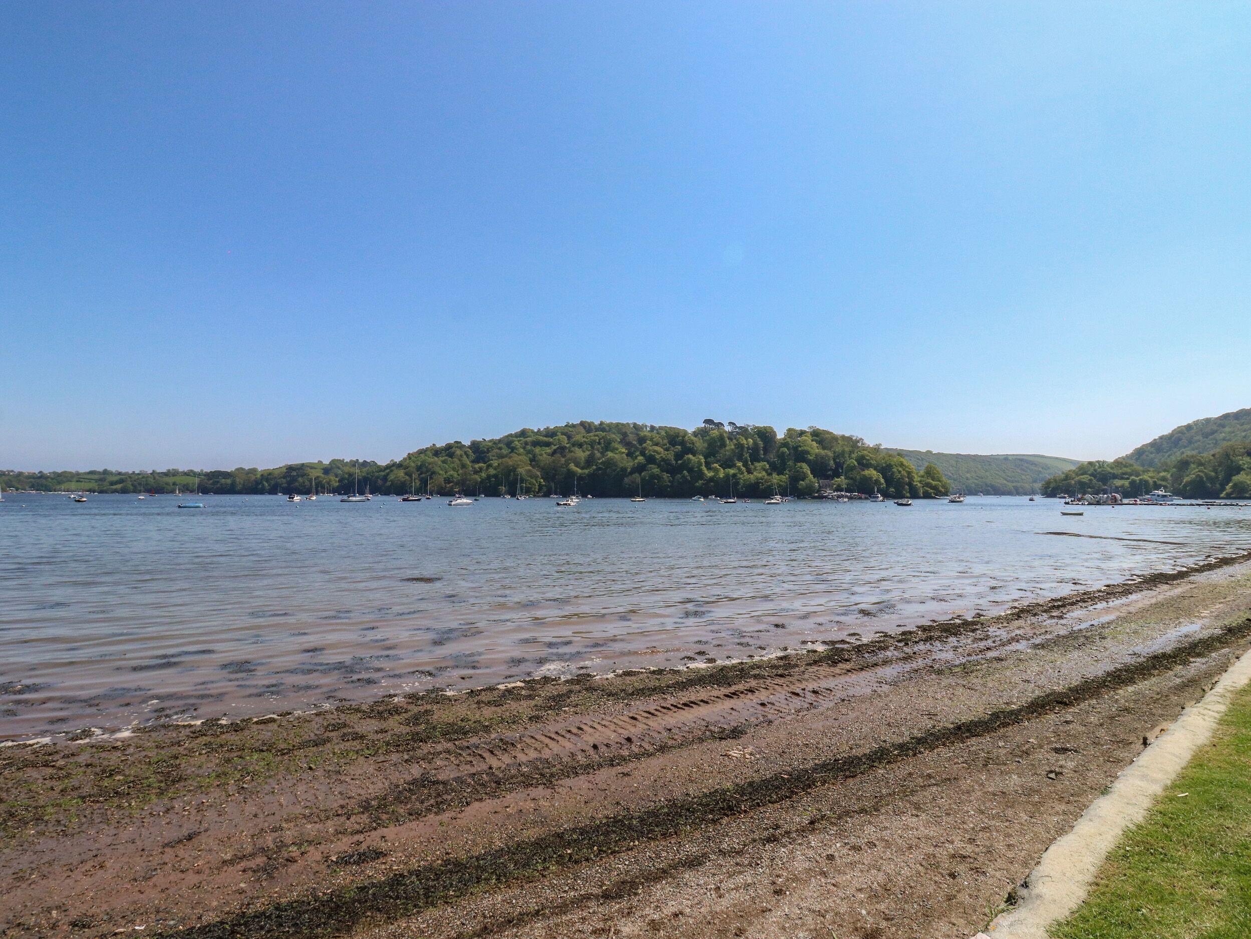 A lakeside view with boats, a sandy beach, and a forested island.