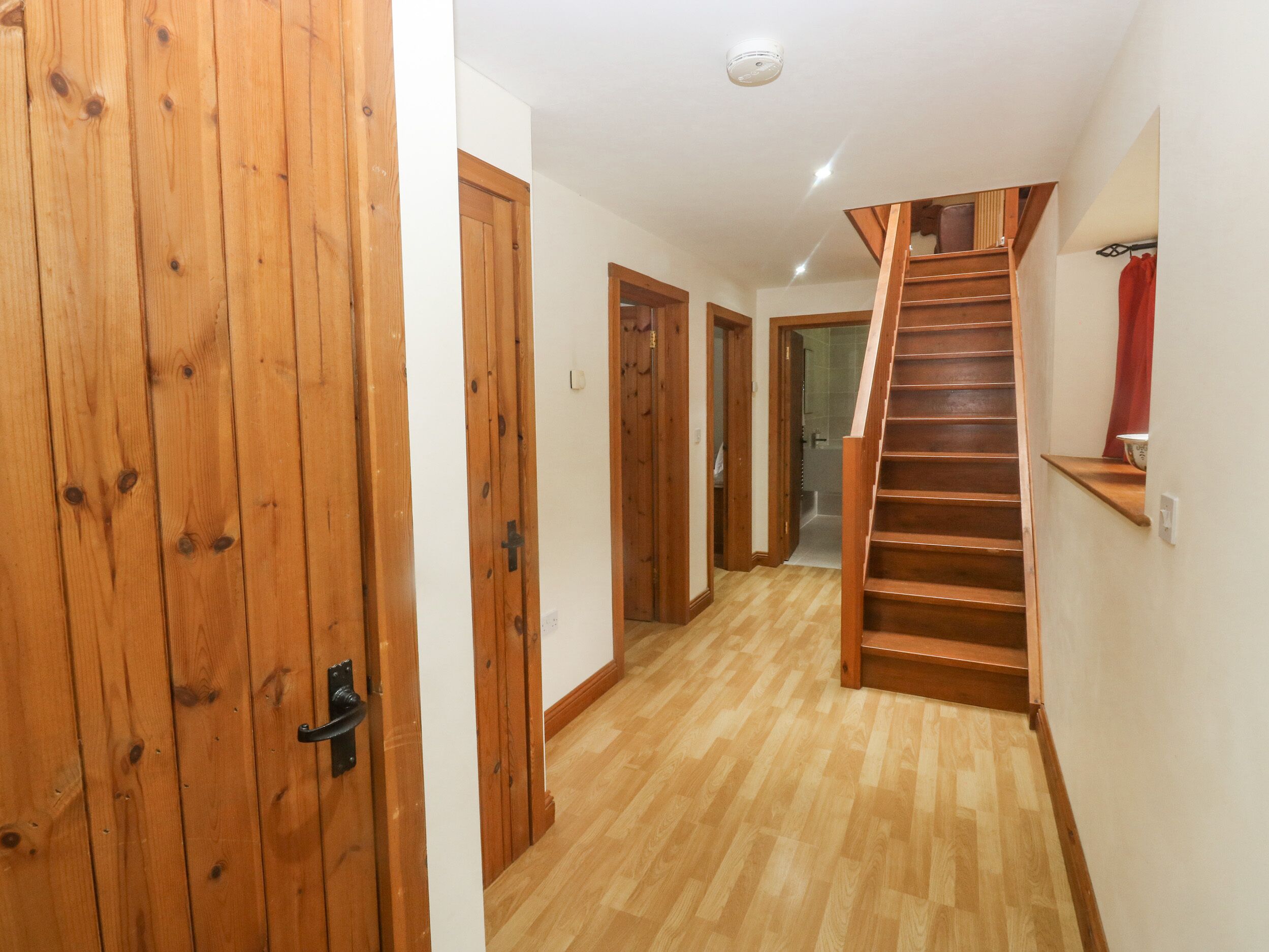 Una escalera de madera que conduce a un segundo piso, una puerta de madera y un pasillo con suelo de madera.