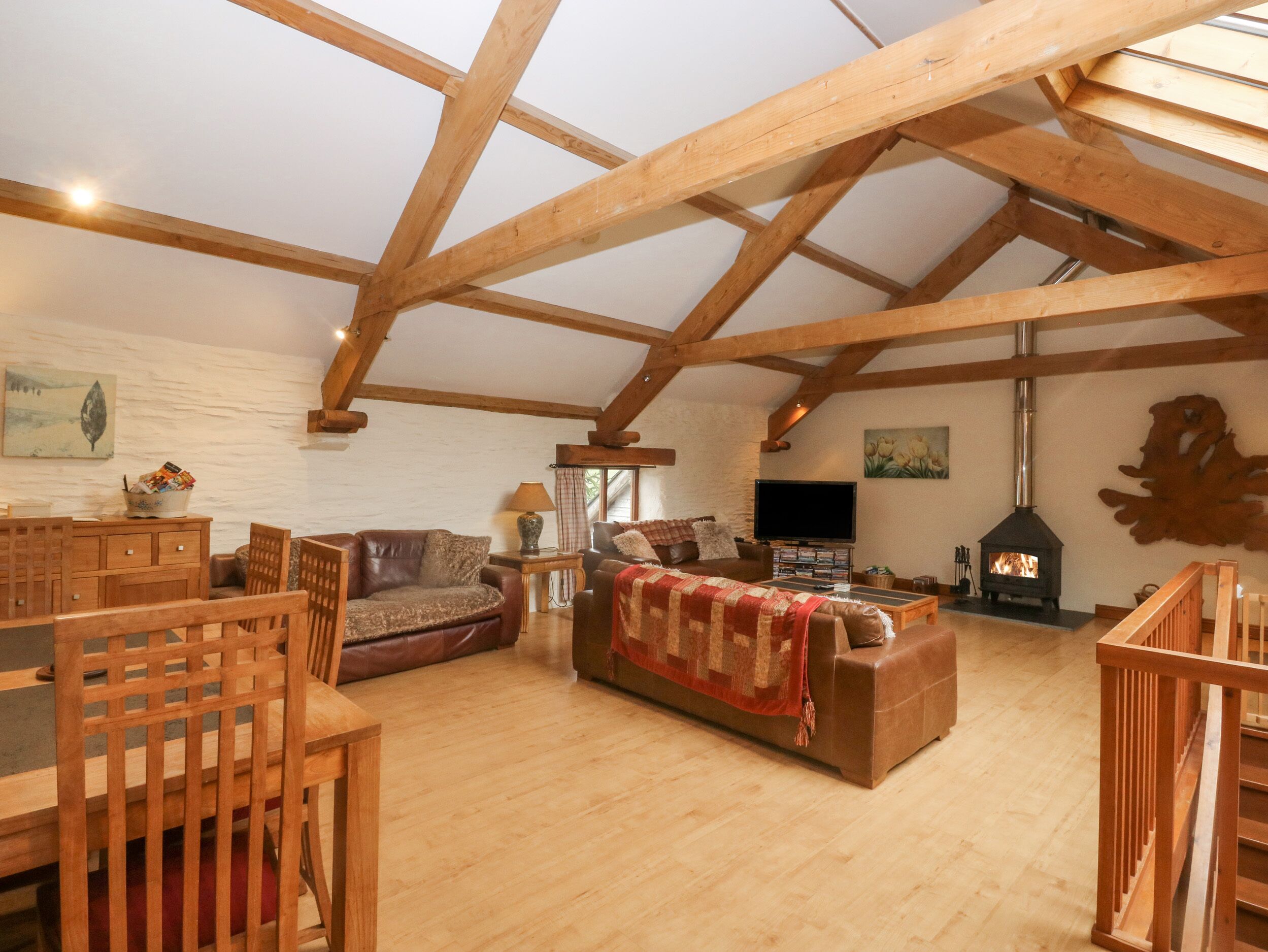 A spacious loft with exposed wooden beams, a fireplace, and a cozy seating area with a sofa and chairs.