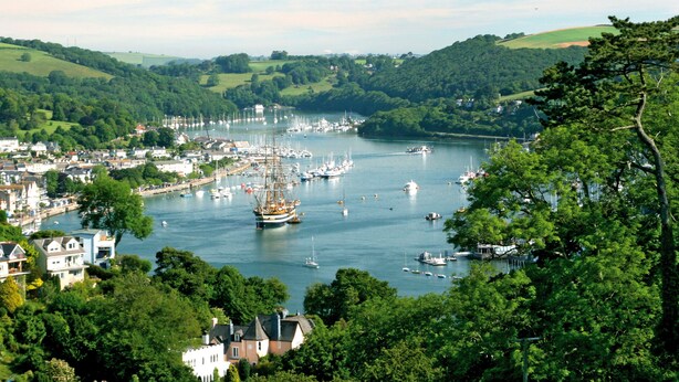 A coastal town with a marina filled with boats, surrounded by lush green hills and residential buildings. - Cowslip Barn (Totnes)