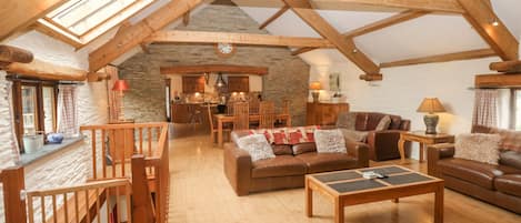 Un loft spacieux avec de hauts plafonds, des poutres apparentes, un mur en pierre et un coin salon confortable agrémenté d’une cheminée.