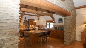 A kitchen with a large island, wooden cabinets, and a stone wall. - Cowslip Barn (Totnes)