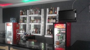 A bar area with shelves of liquor bottles and two refrigerators, one with a red exterior and the other with a black exterior. - Hotel Bison (Nakuru)