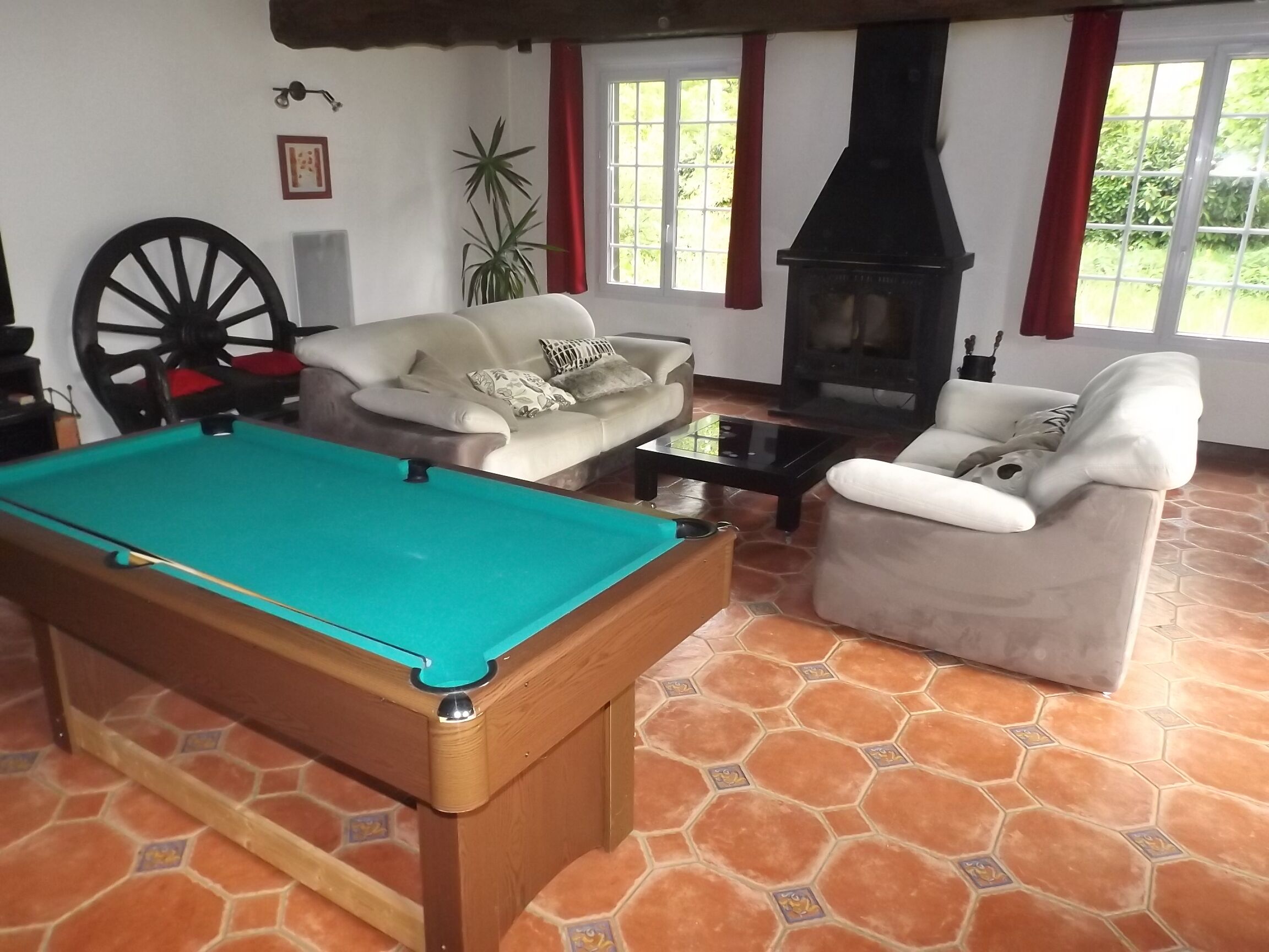 A pool table in a room with a fireplace, two sofas, and a large plant.