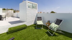 A rooftop terrace with artificial grass, two lounge chairs, a small table, and a white structure with a window. - Puerto del Carmen Vacation Apartment (Puerto del Carmen)