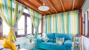 A room with a blue sofa, striped curtains, a hanging light fixture, and a small white table with a vase of flowers. - Puerto del Carmen Vacation Apartment (Puerto del Carmen)