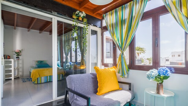A bedroom with a bed, a small table with a vase, and a view of another room through a sliding door. - Puerto del Carmen Vacation Apartment (Puerto del Carmen)