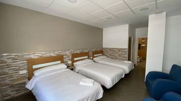 A hotel room with three beds, a blue chair, and a hallway leading to a kitchen area.