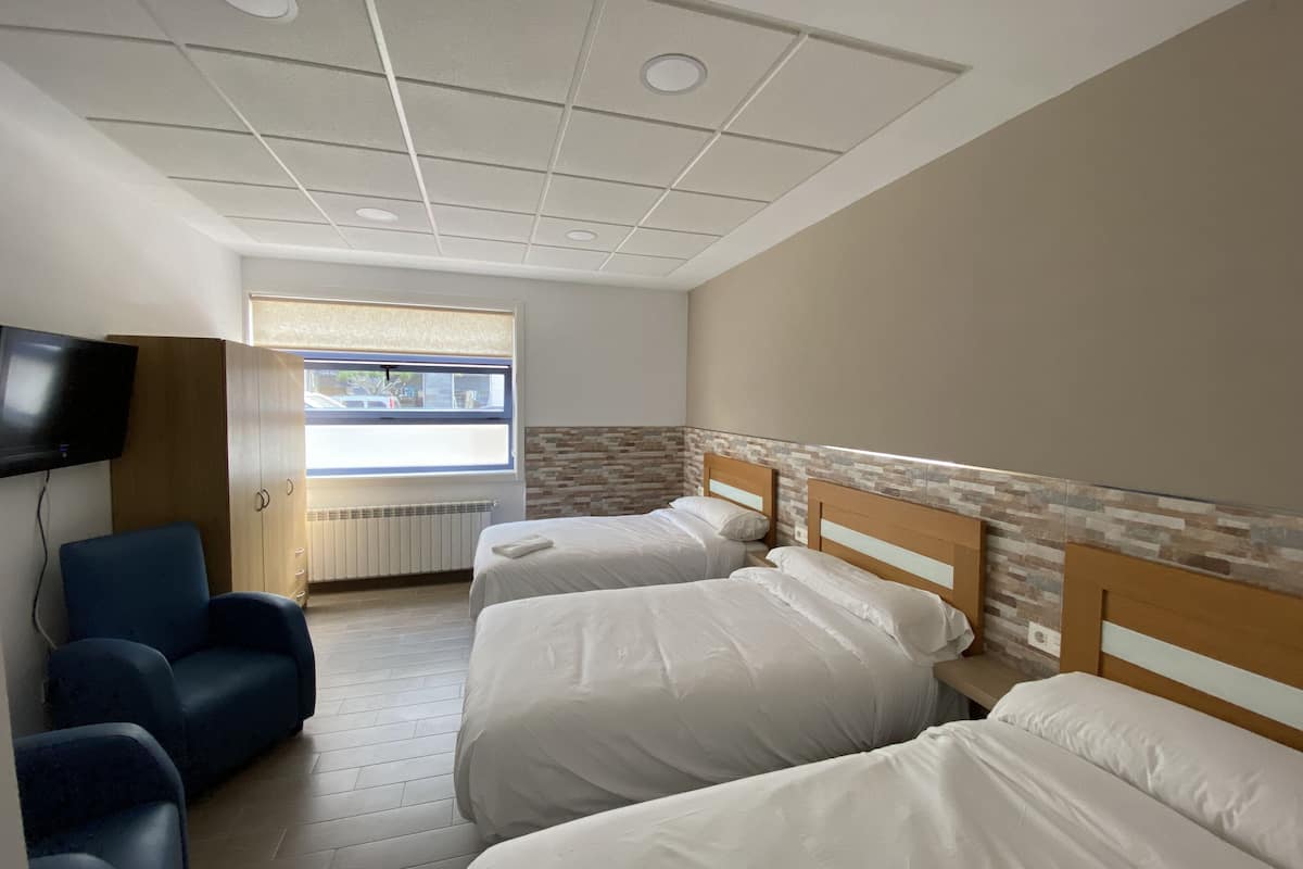 A hotel room with two beds, a TV, a window, and a blue chair.