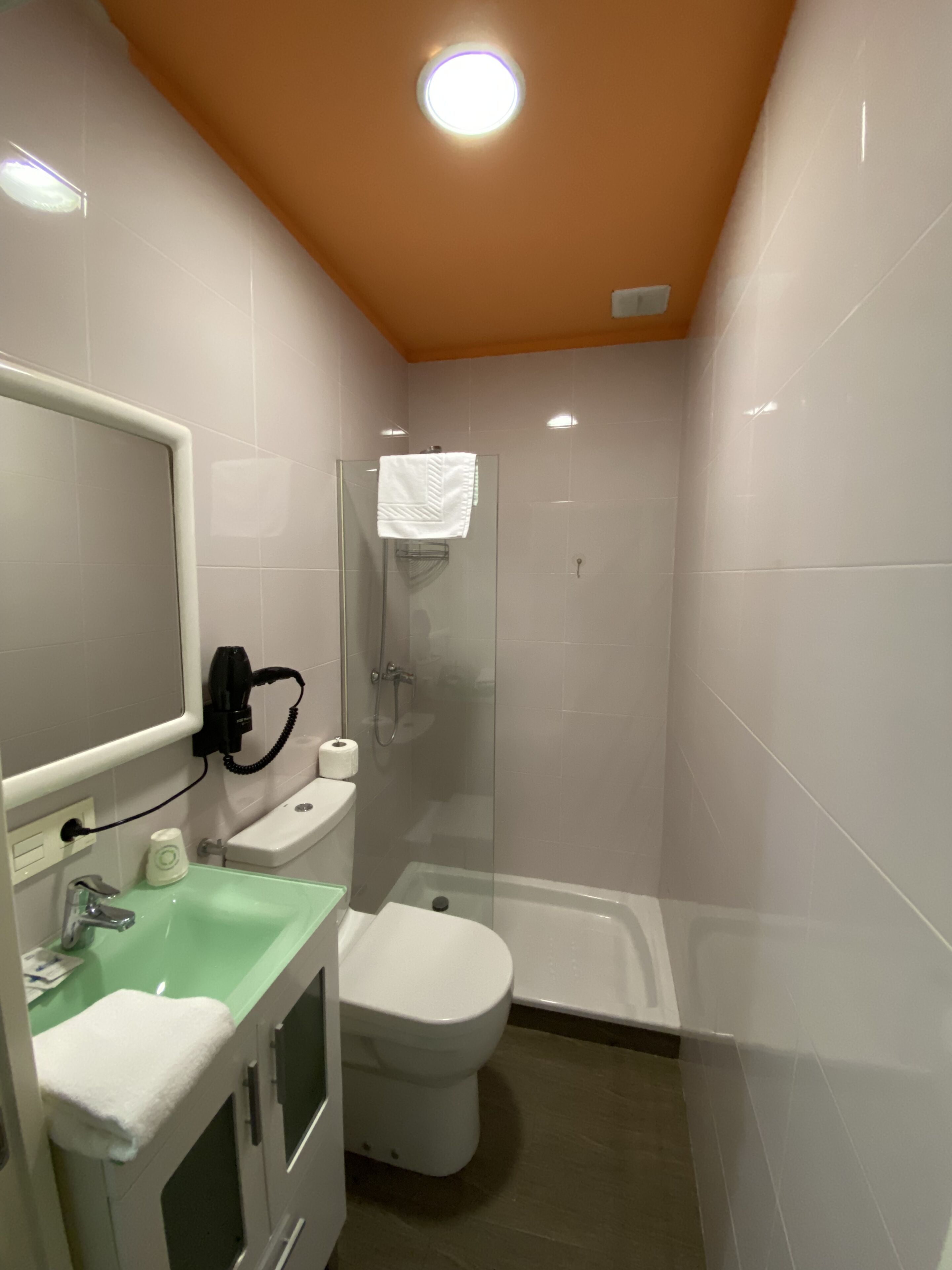 Baño compacto con ducha envuelta en vidrio, inodoro y lavamanos con encimera verde.