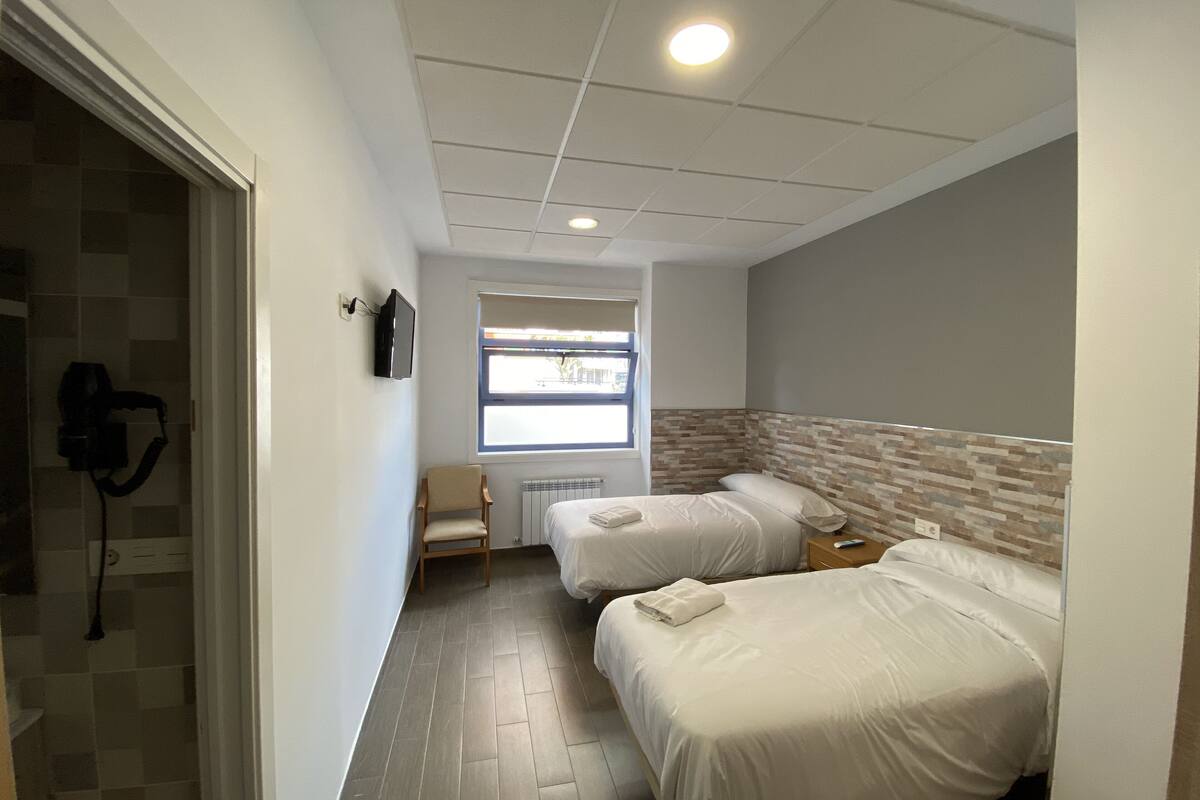 A hotel room with two beds, a TV, a window, and a shower area.