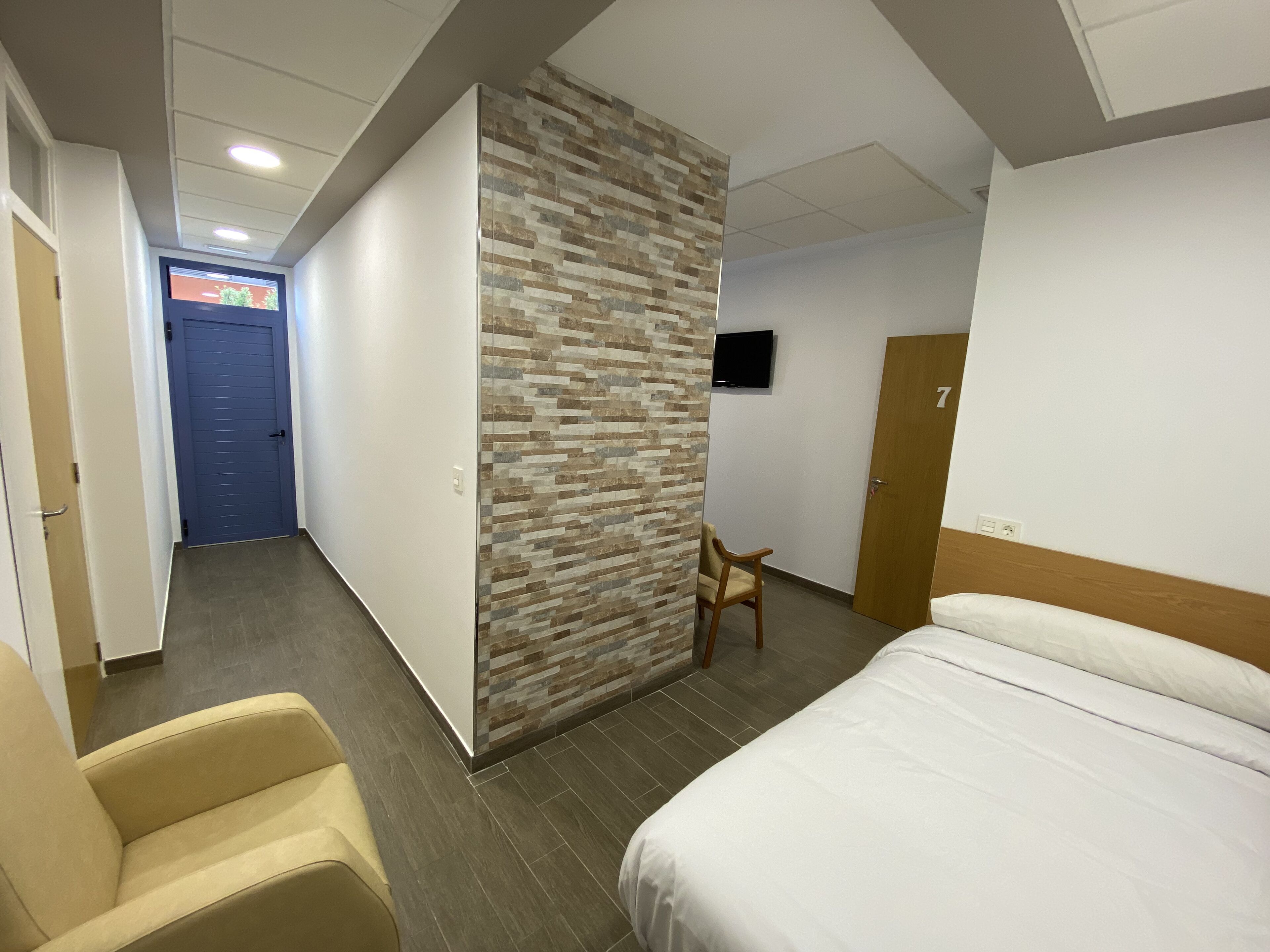 Une chambre d’hôtel avec un lit, une chaise, une télévision et une porte.