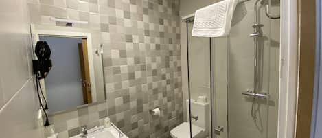Un baño con pared de azulejos, lavamanos, inodoro y ducha con mampara de vidrio.