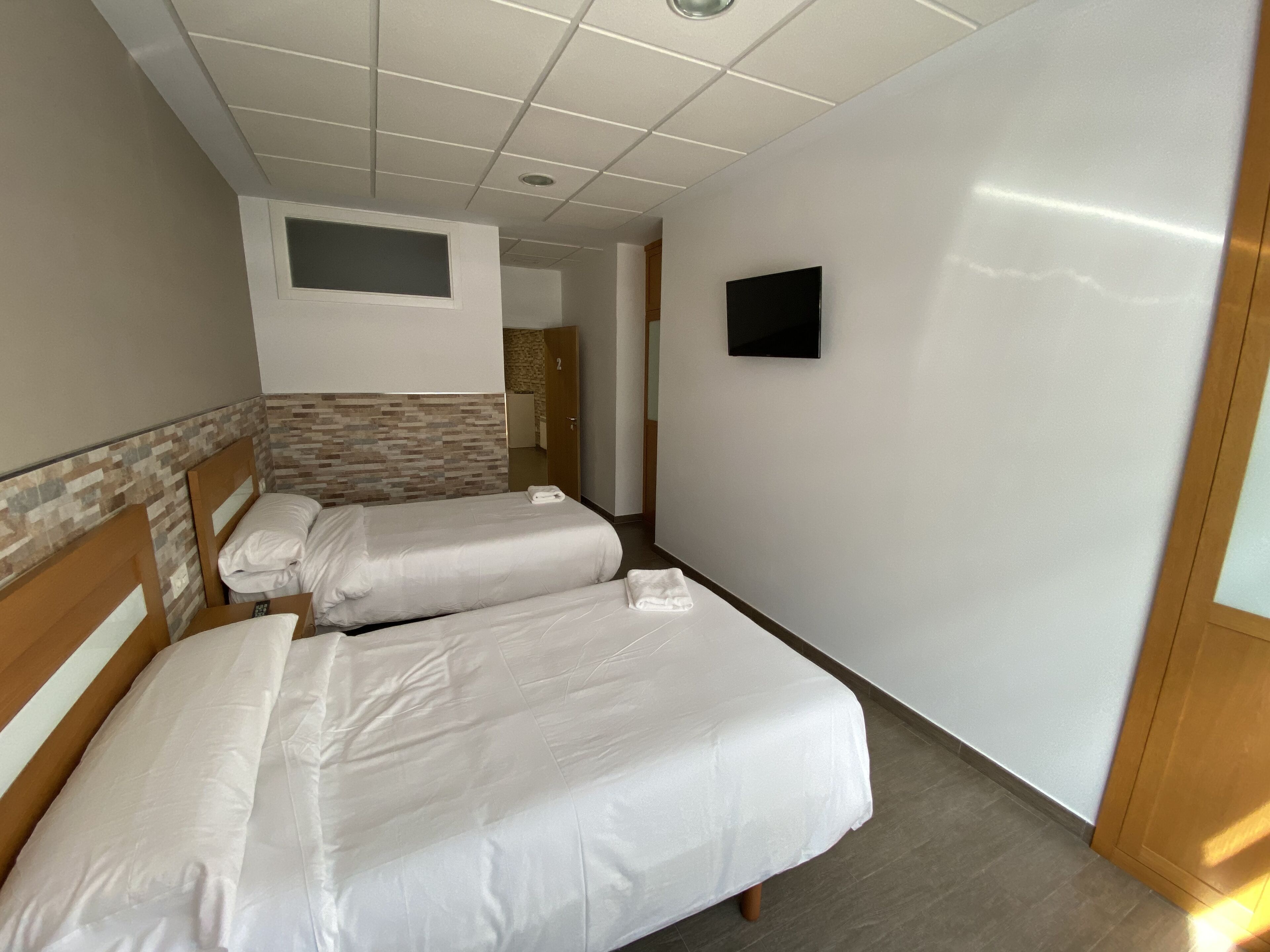 A hotel room with two single beds, a small TV, and a bathroom visible through an open door.
