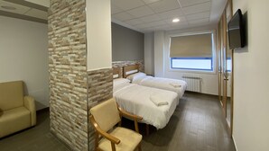 Habitación de hotel con dos camas, una silla de madera, un sofá, un televisor y una ventana con vistas.