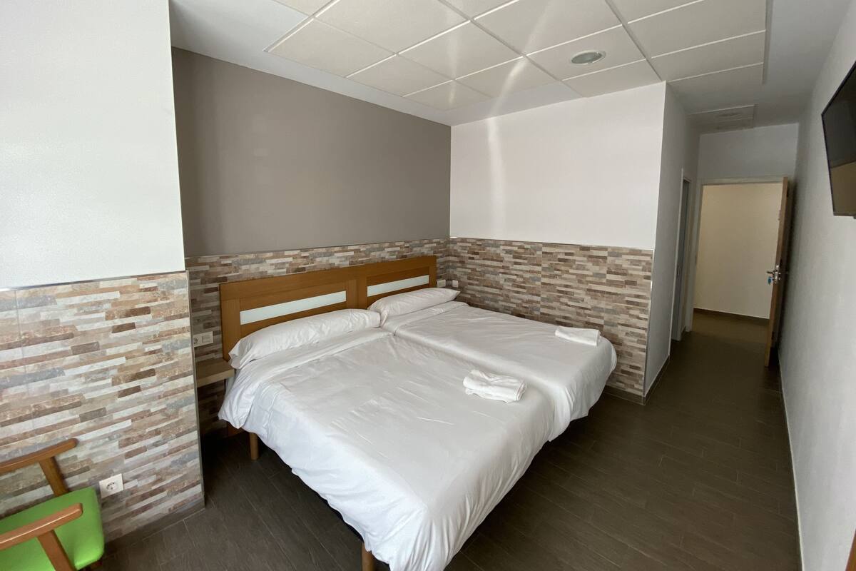 A bedroom with a wooden bed, a green chair, and a tiled ceiling.