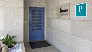 Una puerta azul con teclado de seguridad, un letrero que dice "El Rinconcito de dpCristal" con un símbolo de estacionamiento, y un pequeño jardín con guijarros blancos y una planta.