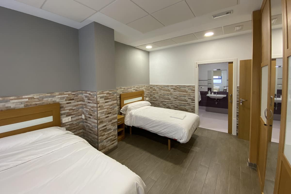 A hotel room with two single beds, a wooden headboard, a small bedside table, and a bathroom visible through an open door.