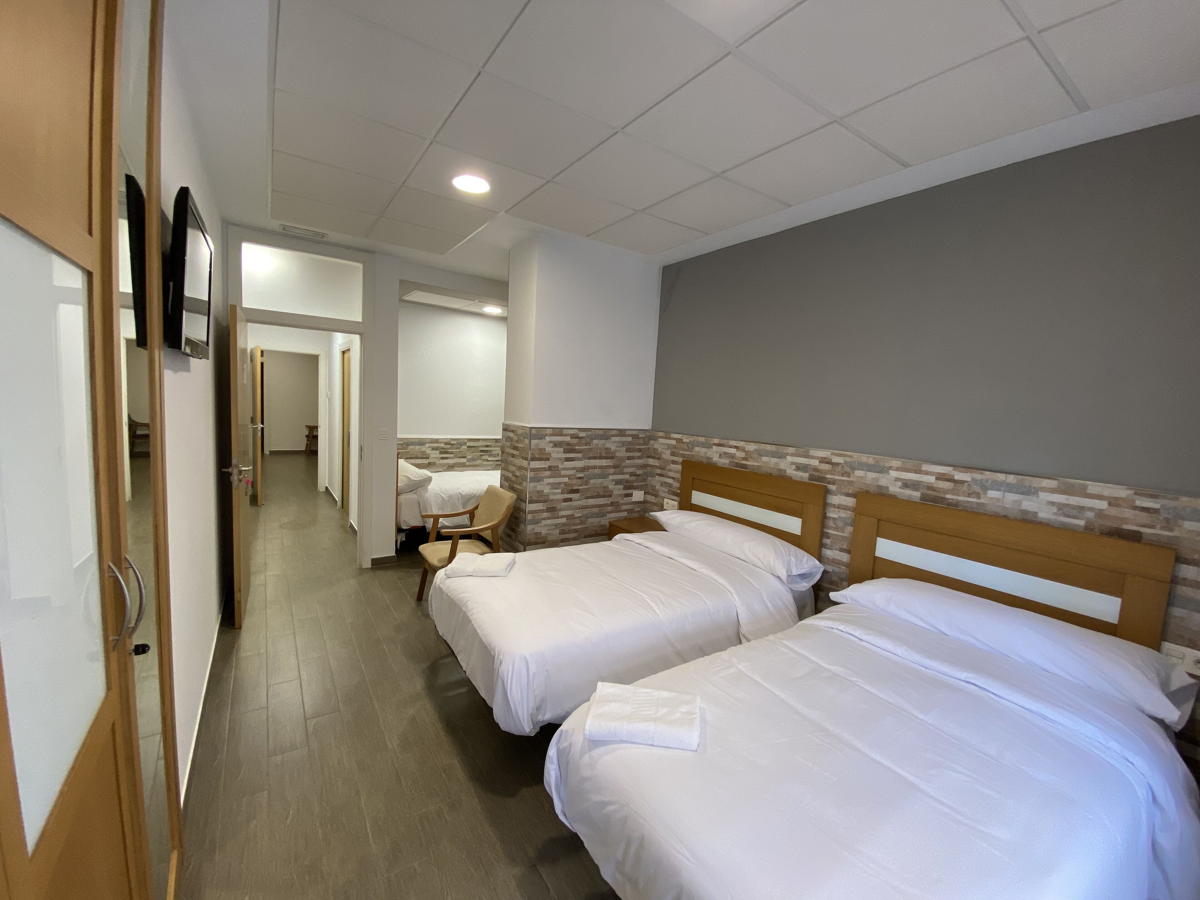 Habitación de hotel con dos camas, cabecero de madera, pared decorativa de azulejos y un pasillo que conduce a otras habitaciones.